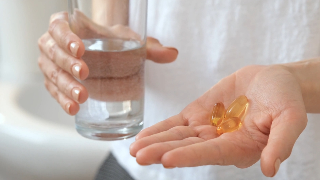 Žena drži kapsule vitamina D u jednoj ruci i čašu vode u drugoj