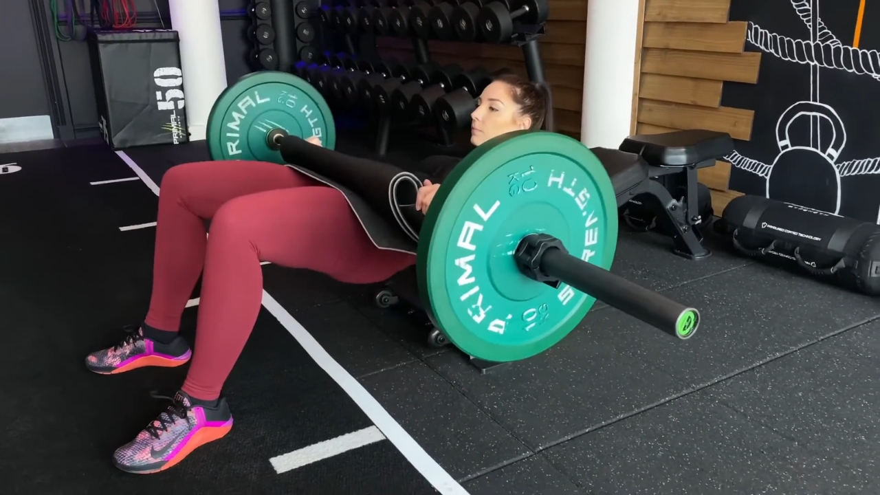 Žena izvodi hip thrust sa šipkom i velikim opterećenjem u teretani